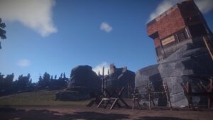 A screenshot from the game Rust, where you can see a base built on top of a cliff, and the base being built of scrap metal. Below the cliff there's barb wire fences.